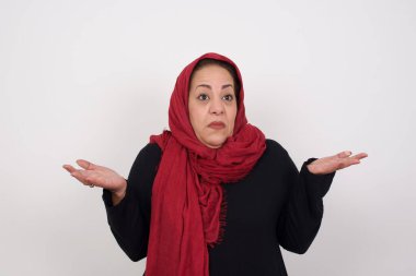 Güzel bir kadın ifadeden şüphe eder, şaşırır ve şaşırır, belirsiz bir gelecek omuz silker, gri duvara karşı durur. Stüdyoda poz veren başörtüsü takan orta yaşlı bir Arap kadın.