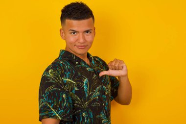 Neşeli, yakışıklı İspanyol adamın yakın çekimi neşeli, memnun ve kendinden emin görünüyor, başparmağıyla işaret ediyor, stüdyo arka planında soyutlanıyor..