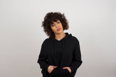 İzole edilmiş arka planda, elleri ceplerinde kameraya bakarken gülümseyen genç ve güzel bir kadın. Pozitif kişi.