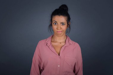 Düşüncelere dalmış, kaşlarını kaldırmış, dudaklarını kıvırmış, şık kıyafetler giymiş, metnin için gri duvarda duran çekici esmer kadın..