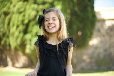 Siyah elbiseli, şık, modern bir kızın yakın portresi. Yumruklarını kaldırıyor, parlak gri arka planda. Büyük gözler ve geniş bir ağız..