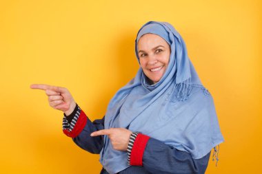 Orta yaşlı tesettürlü çekici Müslüman kadın, neşeli ve ağzı açık şaşırmış ifadesini bir kenara bırakırsak, içeride inanılmaz bir şey gösteriyor. Reklam kavramı.