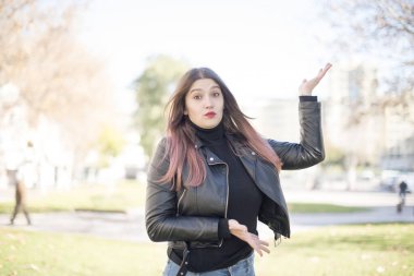 Bahar parkında deri ceket giyen güzel, beyaz tenli bir kadın bir şey gösteriyor.