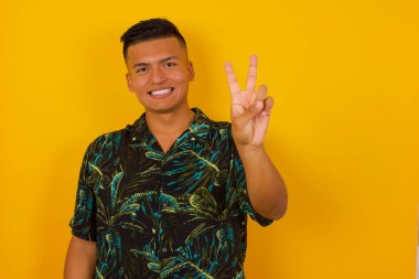 Duvara yaslanmış genç İspanyol adam iki numarayı gösterip işaret ederken kendinden emin ve mutlu bir şekilde gülümsüyor..