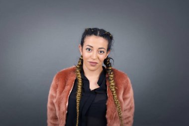 Saçları örgülü güzel bir kadının, gri arka planda poz verirken büyüleyici bir gülümsemeyle kameraya baktığı bir fotoğraf stüdyosu.