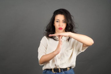 Güzel esmer kadın, gelişigüzel giyinmiş. Gri arkaplanda duruyor. 