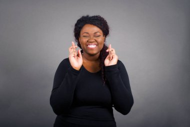 Kazanmak zorundayım. Neşeli, Afro-Amerikalı, sıradan giyinmiş, dişlerini sıkıyor, parmaklarını çapraz yapıyor, arzu edilen dilekleri diliyor, gündelik kıyafetler giyiyor, iyi haberleri bekliyor, gri duvarın üzerinde duruyor.