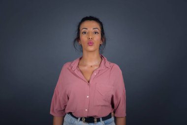 Çekici, açık renk saçlı, yuvarlak dudaklı kadın, doğrudan kameraya bakıyor, tatminini ifade ediyor, gri arka planda izole edilmiş..