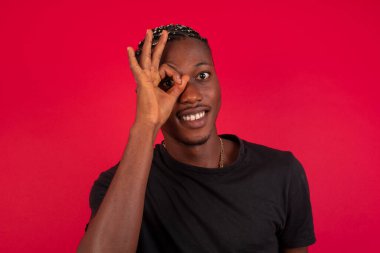 Gülümseyen mutlu yüzlü yakışıklı Afro-Amerikan erkeği el pençe divan durarak işaret veriyor. Sıradan kıyafetler giyip ayakta durmak..