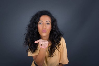 Sevimli bir kadın kameraya yumruk atar, sevgilisine aşkını gösterir ya da uzaktan veda eder, gri stüdyo arka planında izole bir şekilde..