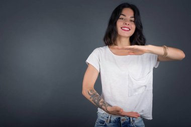 İzole edilmiş arka planda genç ve güzel bir kadın. Elleri büyük ve büyük bir işaret, ölçü sembolü gösteriyor. Kameraya bakıp gülümsüyor. Ölçüm konsepti. 