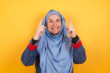 Başarılı, orta yaşlı, tesettürlü, tesettürlü Müslüman bir kadının yatay çekimi. Her iki işaret parmağı da havada, boş bir fotokopi duvarında şok edici bir şey olduğunu gösteriyor..