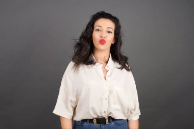 Gri arka planda gelişigüzel giyinmiş güzel esmer kadın öpüşüyor..  