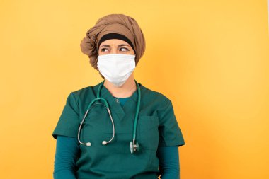 Yeşil üniformalı güzel Müslüman bir kadının fotoğrafı dudaklarını kıvırıyor ve endişeli bir bakış atıyor. Önünde korkunç bir şey görüyor. Arka planda izole edilmiş, tıbbi üniforma giyiyor..