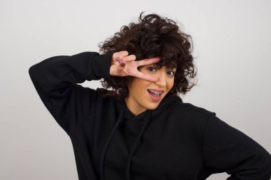 Güzel, güzel bir bayan. Gözlerinin yanında V işareti var. Günlük giysiler giyiyor.