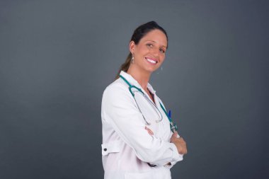 İçerde kolları bağlı duran neşeli, güzel, beyaz bir doktor kadın resmi. Kameraya bakıp gülümsüyor. Kendine güvenen kız..