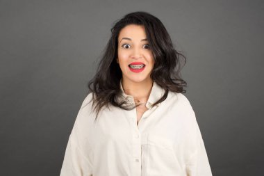 Gayri resmi giyinmiş güzel esmer kadın şaşırdı. Gri arkaplanda duruyor. 