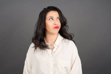Güzel esmer kadın, sıradan giyinmiş, gri arka plana bakıyor..  