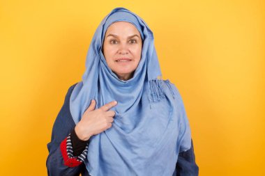 Şaşırmış, orta yaşlı, tesettürlü Müslüman kadın sersemlemiş bir şekilde kendini parmağıyla işaret ederek 