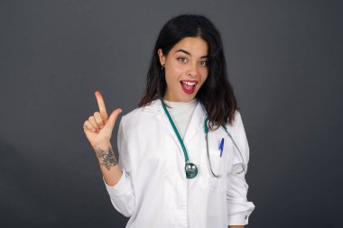 Hoş görünümlü genç doktor kadın modelinin yakın portresi zekice bir ifadeye sahiptir, bir parmağını kaldırır, önemli bir şeyi söylemeyi unutmaması gerektiğini hatırlar. Kapalı