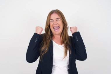 Güzel orta yaşlı kadın mutlu ve heyecanlı kazanan jestler yapıyor. Başarılı ve zaferi kutlayan, muzaffer, gri arka plan.