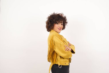 Gri duvara yaslanmış, kolları çaprazlanmış, sıradan kıyafetler giymiş güzel bir bayan. Kameraya bakıp gülümsüyor. Kendine güvenen başarılı bir kadın..