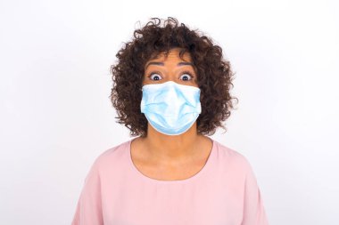  Yüz maskesi takan kafası karışık bir kadın ve beyaz stüdyo arka planında izole edilmiş günlük kıyafetler.