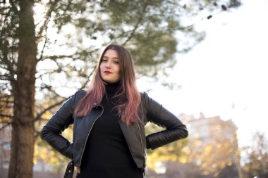 Parkta poz veren deri ceketli beyaz bir kadın.  