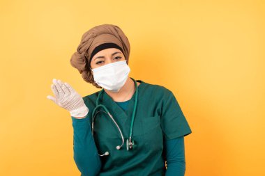 What the hell are you talking about, nonsense. Studio shot of frustrated Young beautiful Muslim doctor woman in green medical uniform  gesturing with raised palm, frowning, being displeased and confused with dumb question over  wall.
