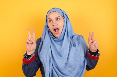 Orta yaşlı tesettürlü neşeli müslüman kadının izole edilmiş çekimi her iki elin de arka planda izole edilmesiyle barış ya da zafer işareti yapıyor.. 