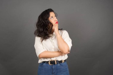 Güzel esmer kadın, sıradan giyinmiş, gri arka plana bakıyor..  