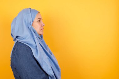 Orta yaşlı, tesettürlü, sağlıklı, saf tenli Müslüman kadının profili, derin düşüncelere dalmış bir ifadeye sahip.