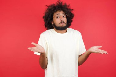 Afro saçlı genç adamın kırmızı duvara karşı kafası karışık.   