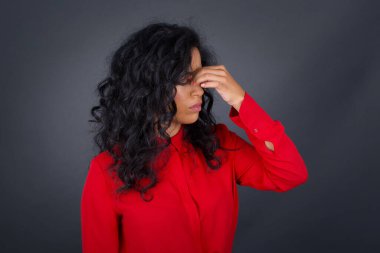 Kıvırcık saçlı, kırmızı tişörtlü çok üzgün bir kadın açık havada dururken burnuna dokunuyor, ağlamak istiyor, stresli bir ilişkisi var, sevgilisiyle anlaşmazlık yaşıyor, işiyle ilgili sorunları var.