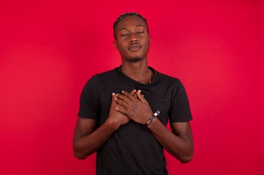 Kırmızı arka plan üzerine siyah t-shirt giyen Afro-Amerikalı bir adam gözlerini kapatır ve ellerini kalbine yakın tutar, nezaketini ya da iyiliğini gösterir, samimi duygularını ifade eder, iyi kalpli ve dürüst olur. Vücut dili ve gerçek duygular kavramı