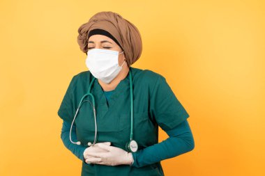 Steteskoplu kadın doktor ve yüz maskesi stüdyoda karın ağrısı var.