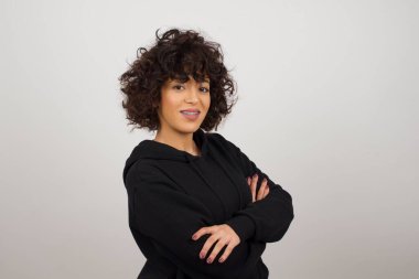 Kollarını kavuşturmuş neşeli, beyaz bir kadının görüntüsü. Kameraya bakıp gülümsüyor. Kendine güvenen kız..