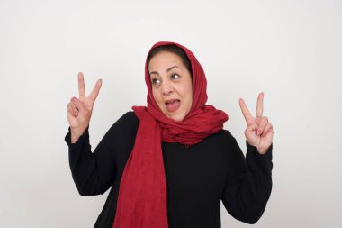 Neşeli, olgun Müslüman bir kadının yalnız çekimi iki eliyle barış ya da zafer işareti yapar.