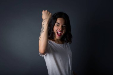 Sevinçten havalara uçmuş mutlu, sevinçli bir kadın, iyi haberler aldığına sevinmiş, mutluluktan hareketler yapmış, yumruğunu sıkmış ve kazanan bir jest yapmış. Tepki konsepti.