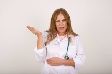 What the hell are you talking about, nonsense. Studio shot of frustrated  mature caucasian doctor woman in lab coat gesturing with raised palm, frowning, being displeased and confused with dumb question over gray wall.
