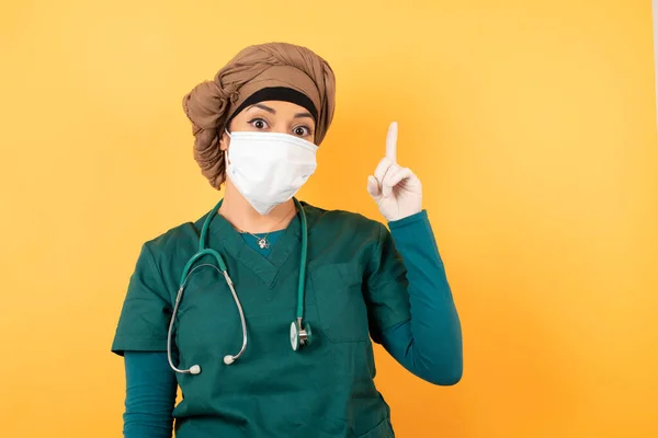 緑色の医学の制服の若い美しいイスラム教徒の医師の女性のクローズアップの肖像画は 一つの指を指して 見上げて笑顔 私はアイデアを持っています 私は答えを知っているか 解決策を知っています — ストック写真