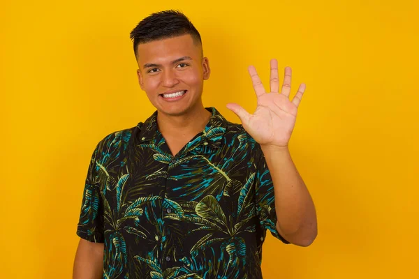 Genç İspanyol adam duvarın önünde duruyor ve beş numarayı gösterip işaret ederken kendinden emin ve mutlu bir şekilde gülümsüyor..