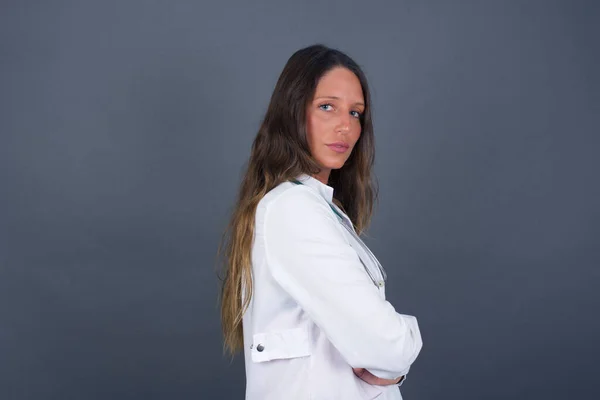 Profile of doctor woman with healthy pure skin has braided hairstyle wears black clothes has contemplative expression ready to have outdoor walk isolated over grey studio wall with copy space.