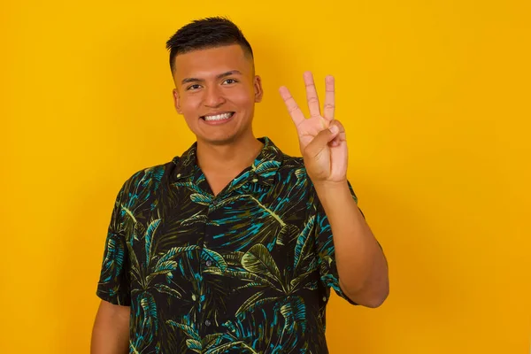 Duvara yaslanmış genç İspanyol adam üç numarayı gösterip işaret ederken kendinden emin ve mutlu gülümsüyor..