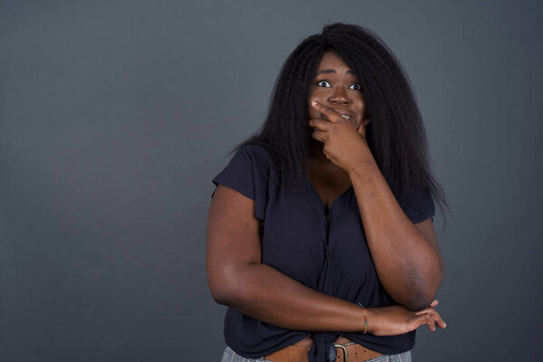 Anxiety - a conceptual image of a beautiful African American woman covering her mouth with her hands and standing indoors. Scared from something or someone bite nails