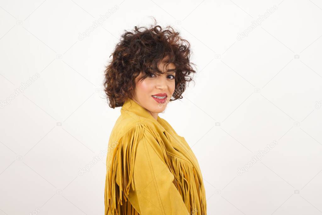 Shy girl smiling looking to the camera. Caucasian charming girl sanding against gray studio background feeling shy.