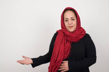 Güzel bir kadının portresi. Gri arka planda hoş geldin jesti. Stüdyoda poz veren başörtüsü takan orta yaşlı bir Arap kadın.