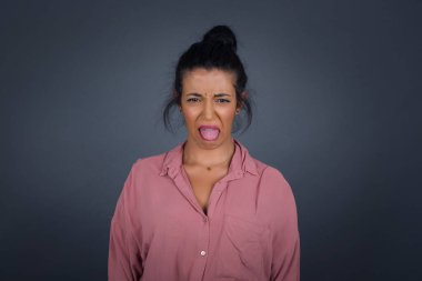 Gri duvara karşı poz veren, suratını asan, bir şeye karşı hoşnutsuzluk gösteren, düz saçlı, stresli, güzel bir kız..