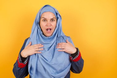 Korkmuş orta yaşlı Müslüman kadın ellerini göğsünde tutuyor, ağzı açık, kameraya bakıyor. 