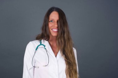 Güzel görünümlü beyaz bir kadının yatay portresi gri arka planda izole edilmiş, uzun, güzel saçları olan, yüzünü saçlarıyla örten ve kameraya mutlu bir şekilde bakan bir kadın..